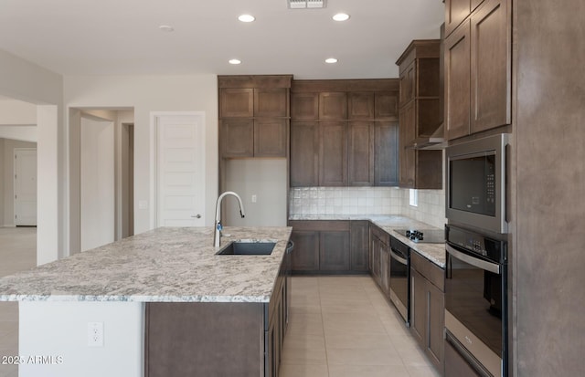 kitchen with a center island with sink, stainless steel microwave, backsplash, wall oven, and a sink