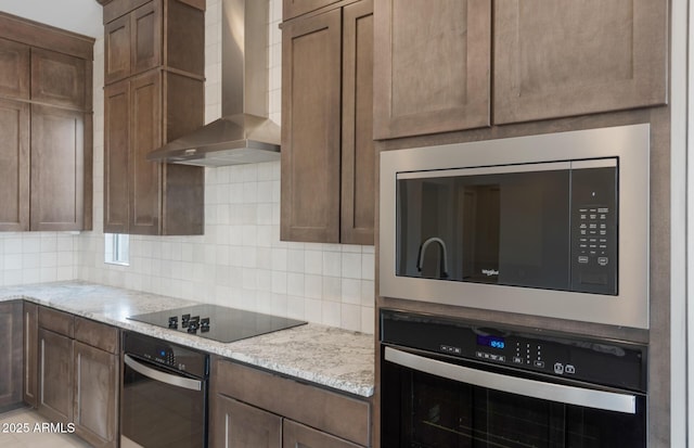 kitchen featuring black appliances, light stone counters, wall chimney exhaust hood, and backsplash