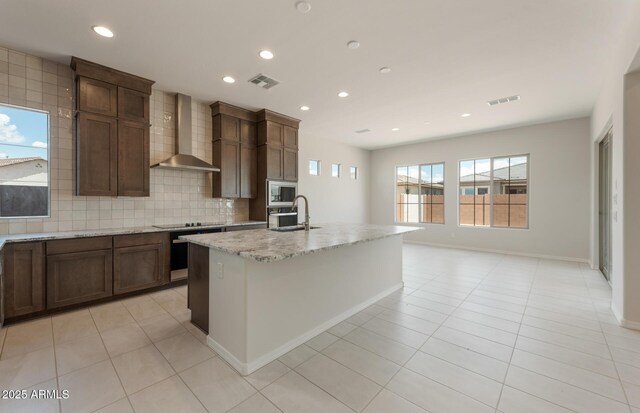 kitchen featuring visible vents, backsplash, a sink, wall chimney range hood, and built in microwave