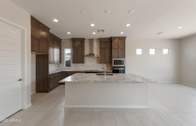 kitchen with a center island with sink, visible vents, wall chimney exhaust hood, stainless steel microwave, and a sink