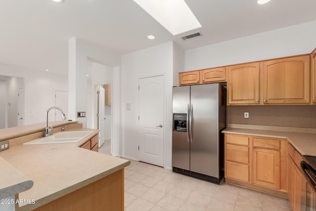 kitchen featuring visible vents, light countertops, a skylight, stainless steel refrigerator with ice dispenser, and a sink