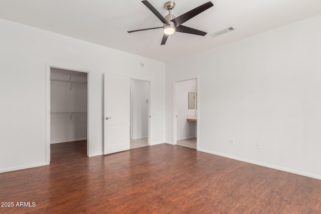 unfurnished bedroom featuring visible vents, wood finished floors, a closet, baseboards, and a spacious closet