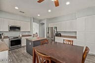 kitchen featuring ceiling fan, a kitchen island with sink, appliances with stainless steel finishes, and white cabinetry