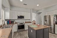 kitchen featuring a kitchen island, sink, light wood-type flooring, stainless steel appliances, and white cabinets