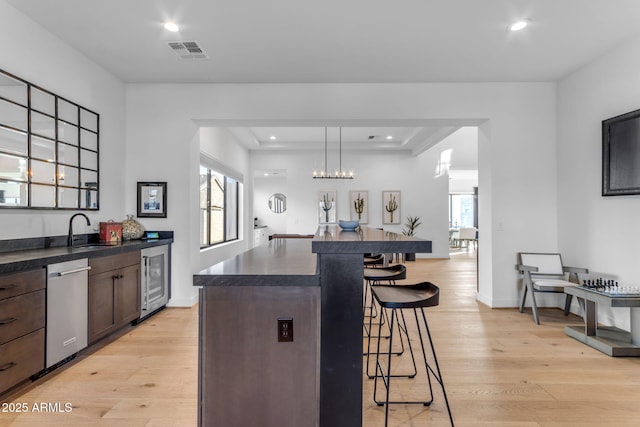 kitchen featuring light wood-type flooring, dark brown cabinetry, dishwasher, hanging light fixtures, and a breakfast bar area