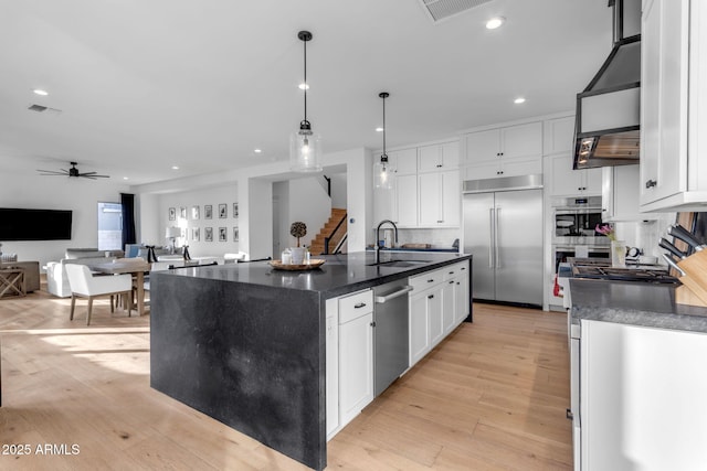 kitchen featuring pendant lighting, a kitchen island with sink, sink, appliances with stainless steel finishes, and white cabinetry