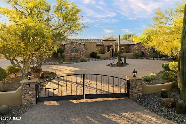 view of front of home featuring stone siding, stucco siding, a gate, a fenced front yard, and a tile roof