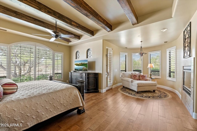 bedroom with baseboards, multiple windows, beam ceiling, and wood finished floors