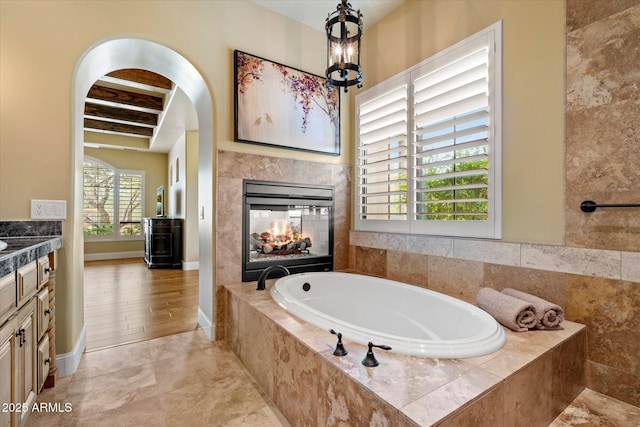 bathroom with a garden tub, a multi sided fireplace, baseboards, and vanity