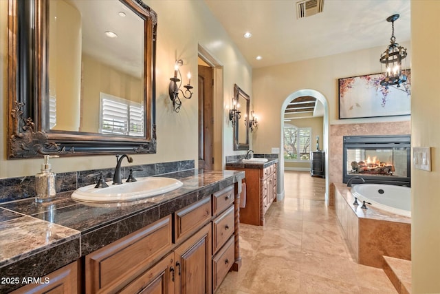 bathroom with visible vents, a garden tub, two vanities, a sink, and a multi sided fireplace