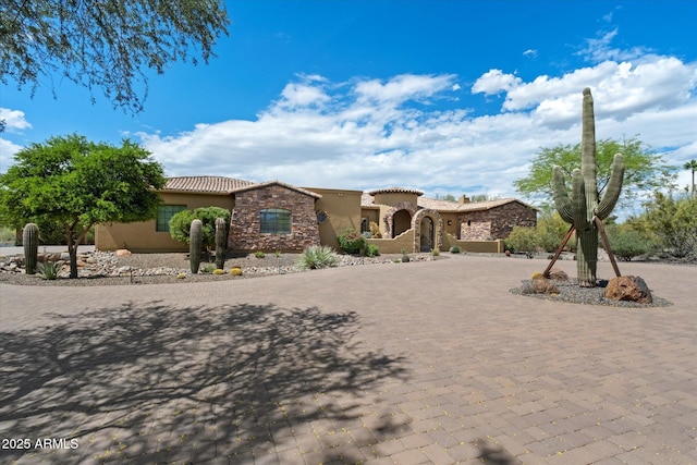 mediterranean / spanish-style house with a tiled roof, curved driveway, stone siding, and stucco siding