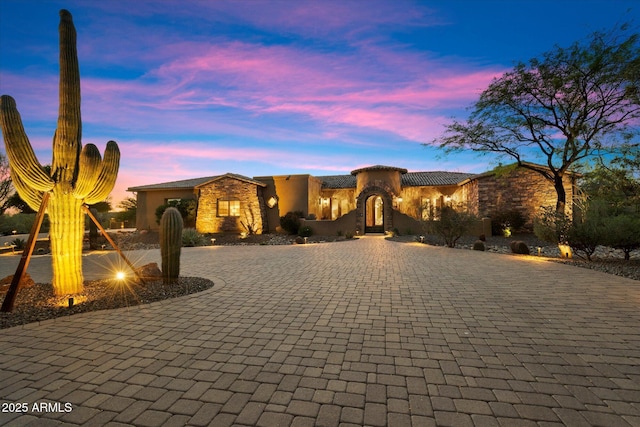 view of front of property with curved driveway, stucco siding, a tile roof, and stone siding