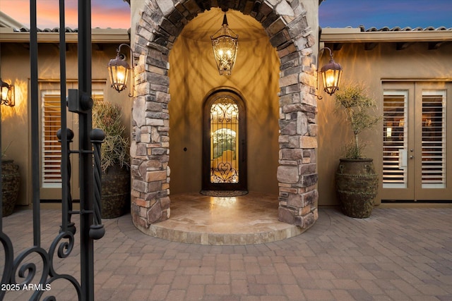 property entrance with french doors, stucco siding, and stone siding
