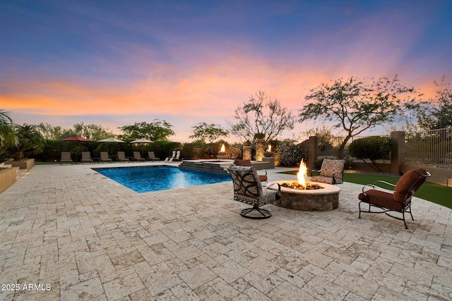 pool at dusk featuring a fenced backyard, a patio, a pool with connected hot tub, and an outdoor fire pit