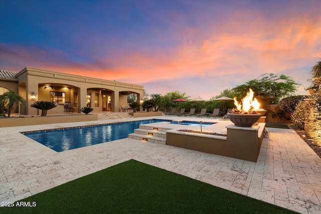 pool at dusk with a fenced in pool, a patio, an in ground hot tub, and an outdoor fire pit