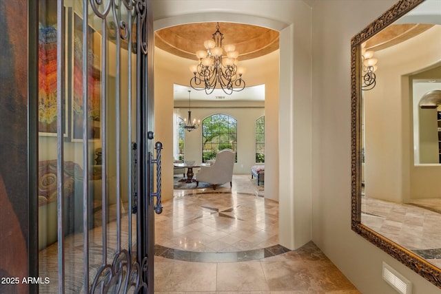 foyer entrance with a raised ceiling, tile patterned floors, a notable chandelier, and visible vents