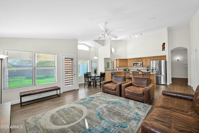 living room featuring high vaulted ceiling, a ceiling fan, wood finished floors, arched walkways, and baseboards