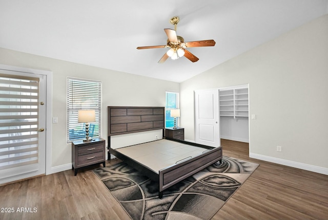 bedroom with a spacious closet, vaulted ceiling, baseboards, and wood finished floors