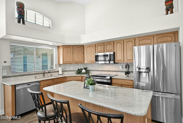 kitchen with backsplash, light stone countertops, appliances with stainless steel finishes, a kitchen breakfast bar, and a sink