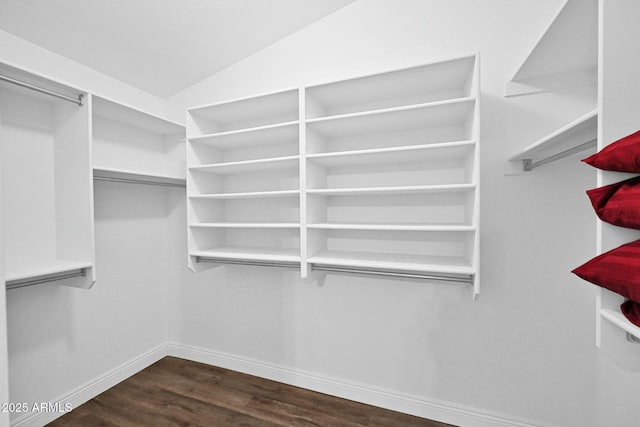 spacious closet with dark wood finished floors and vaulted ceiling