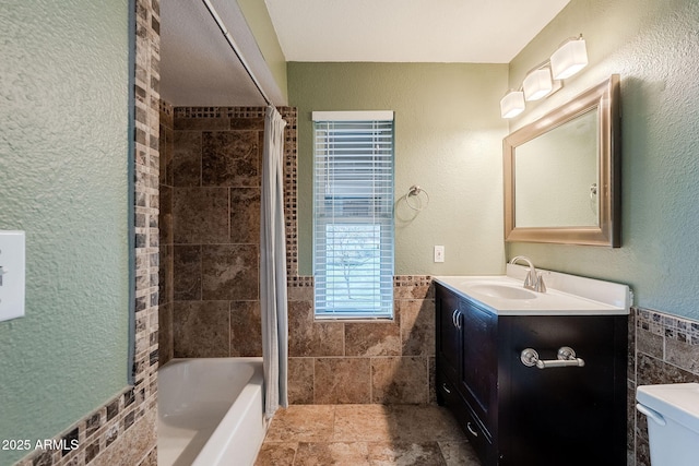 full bathroom with vanity, toilet, tiled shower / bath combo, and tile walls