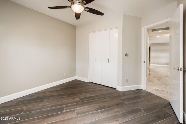 unfurnished bedroom featuring ceiling fan, baseboards, dark wood finished floors, and a closet