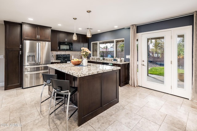 kitchen with light stone counters, a center island, tasteful backsplash, dark brown cabinets, and black appliances