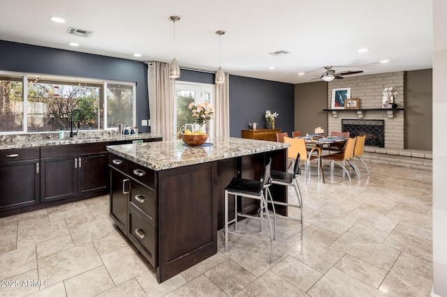 kitchen featuring a kitchen bar, visible vents, a fireplace, and light stone counters