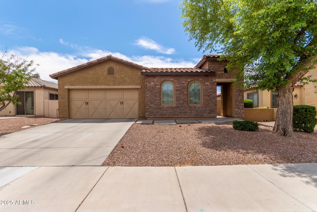 mediterranean / spanish home with a tile roof, driveway, stone siding, an attached garage, and stucco siding