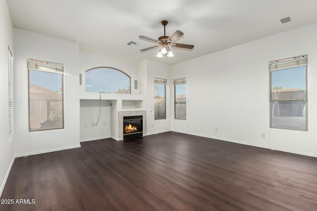 unfurnished living room featuring a tiled fireplace, dark wood-type flooring, a wealth of natural light, and ceiling fan