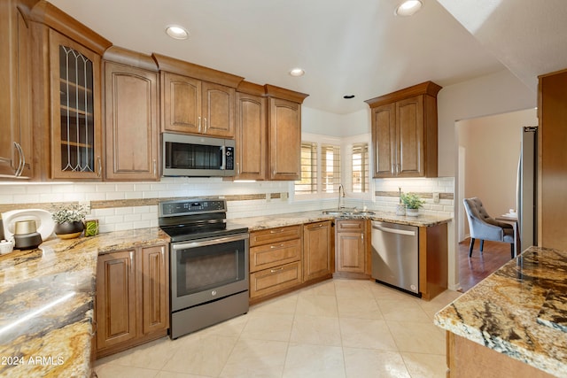 kitchen with light stone counters, tasteful backsplash, light tile patterned floors, stainless steel appliances, and sink