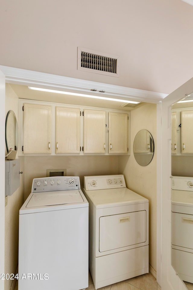 clothes washing area featuring cabinets, light tile patterned floors, and washing machine and clothes dryer