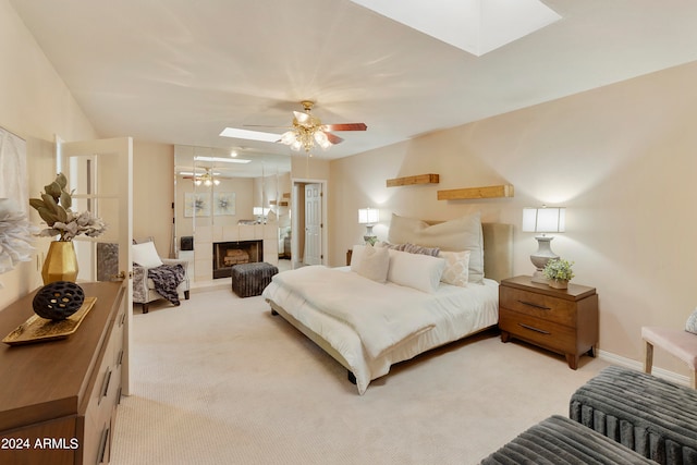 carpeted bedroom featuring a tiled fireplace, ceiling fan, and a skylight