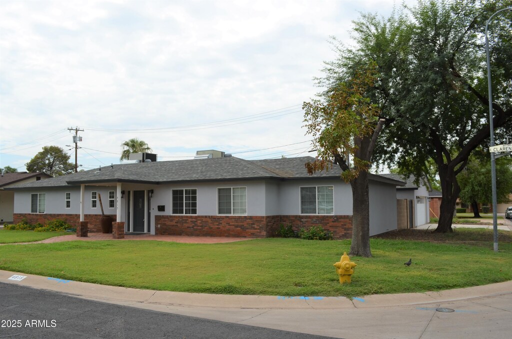 single story home with stucco siding, an attached garage, a front lawn, brick siding, and a shingled roof