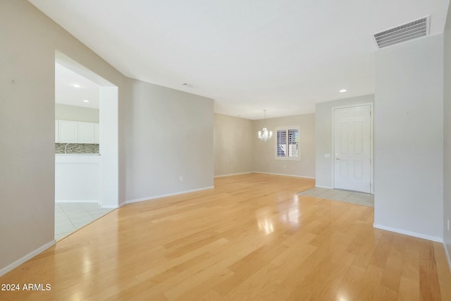 spare room with light hardwood / wood-style floors and an inviting chandelier