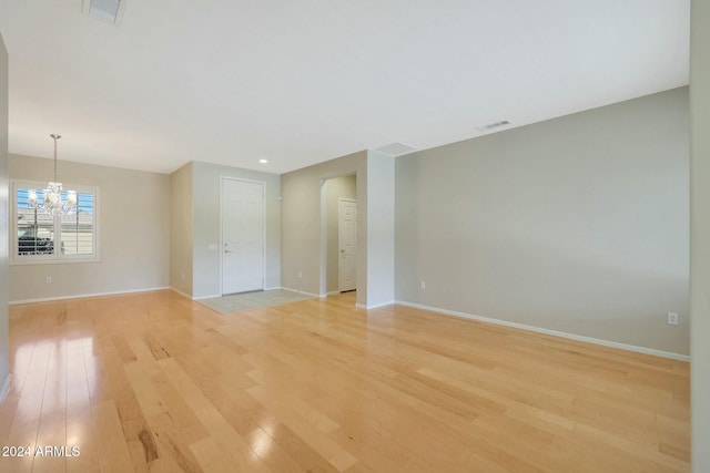 empty room featuring light wood-type flooring and an inviting chandelier