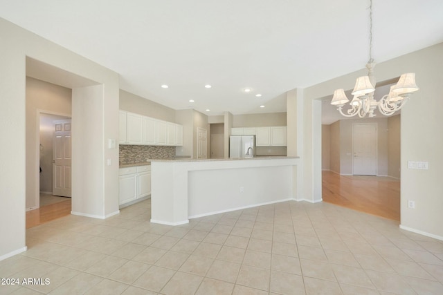 kitchen with an inviting chandelier, white fridge, pendant lighting, decorative backsplash, and white cabinets