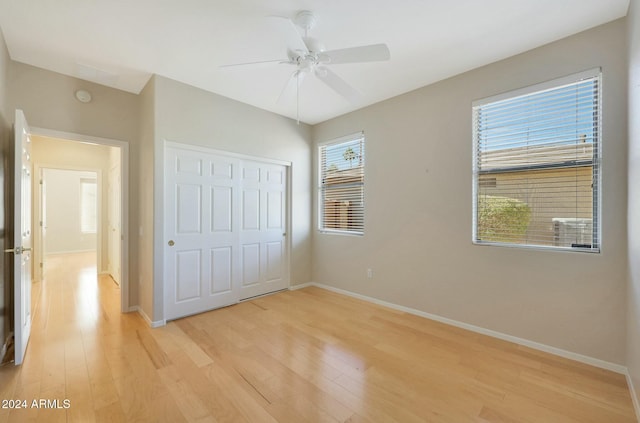 unfurnished bedroom featuring ceiling fan, light hardwood / wood-style floors, multiple windows, and a closet