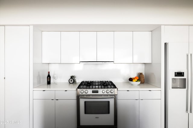 kitchen with white cabinetry, light countertops, white fridge with ice dispenser, and stainless steel gas range oven