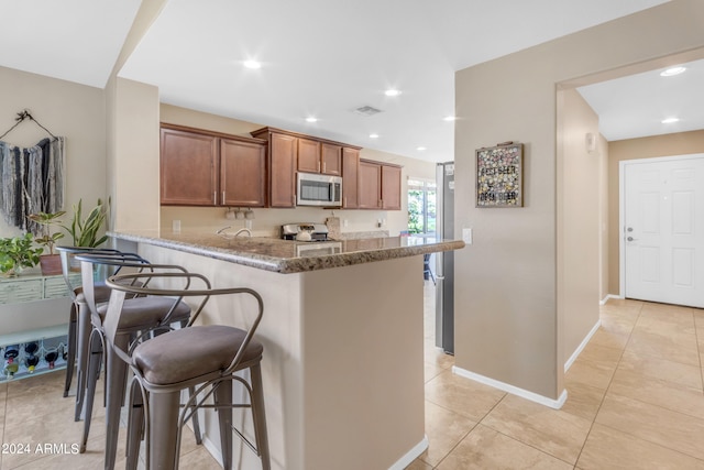 kitchen with light tile patterned flooring, a breakfast bar area, light stone counters, kitchen peninsula, and stainless steel appliances