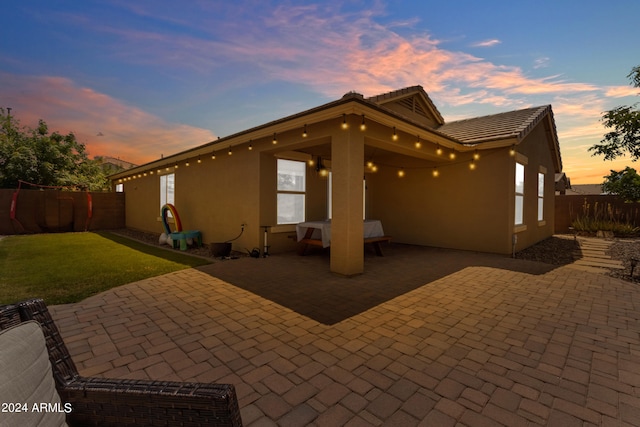 back house at dusk with a patio and a lawn