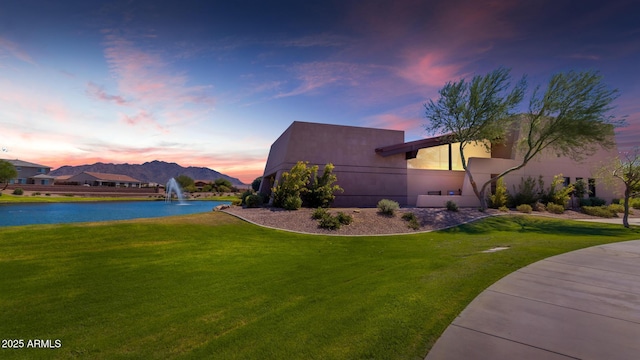 property exterior at dusk with a water view and a yard