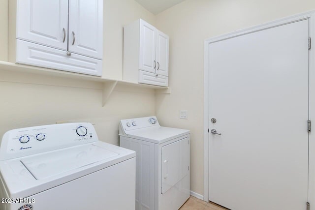 washroom featuring washing machine and dryer, light tile patterned flooring, and cabinets