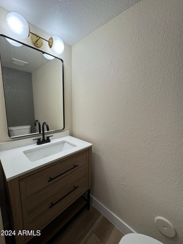 bathroom with wood-type flooring, a textured ceiling, toilet, and vanity