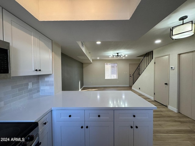 kitchen with white cabinets, tasteful backsplash, electric stove, kitchen peninsula, and light hardwood / wood-style flooring