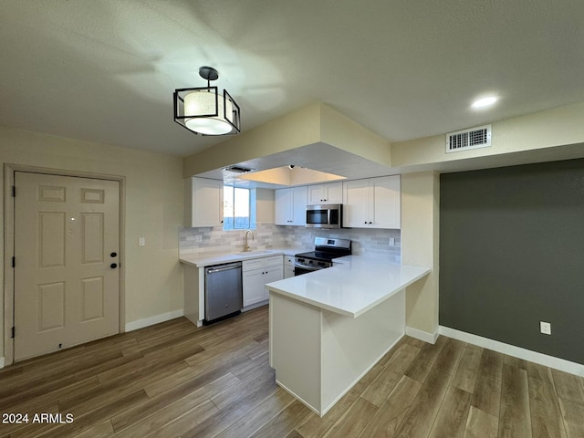 kitchen featuring white cabinets, appliances with stainless steel finishes, decorative light fixtures, decorative backsplash, and kitchen peninsula