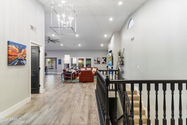 hall featuring a towering ceiling, light hardwood / wood-style floors, and a notable chandelier