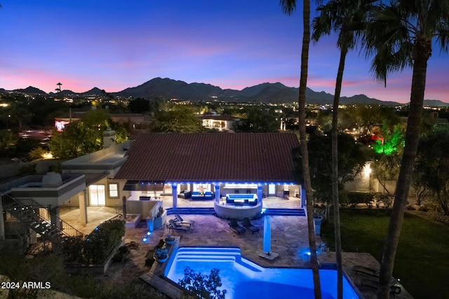 pool at dusk featuring a mountain view, a patio, and an in ground hot tub