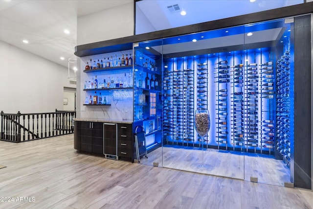 bar featuring light stone countertops, light wood-type flooring, and a towering ceiling