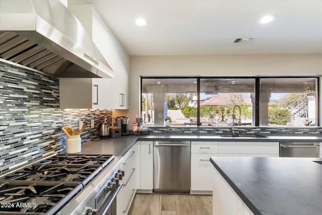 kitchen with a wealth of natural light, white cabinets, wall chimney range hood, and appliances with stainless steel finishes